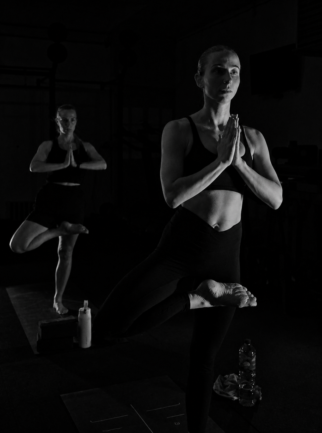 Two students holding tree pose in the low-lit BLACKOUT studio
